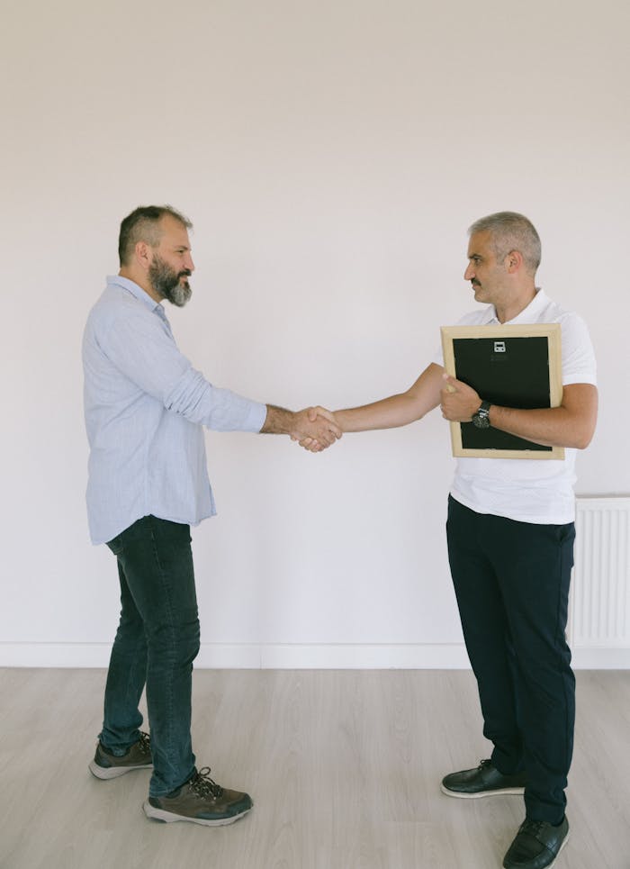 Man In White Shirt And Black Pants Shaking Hands With Man In Blue Long Sleeve Shirt 8978560
